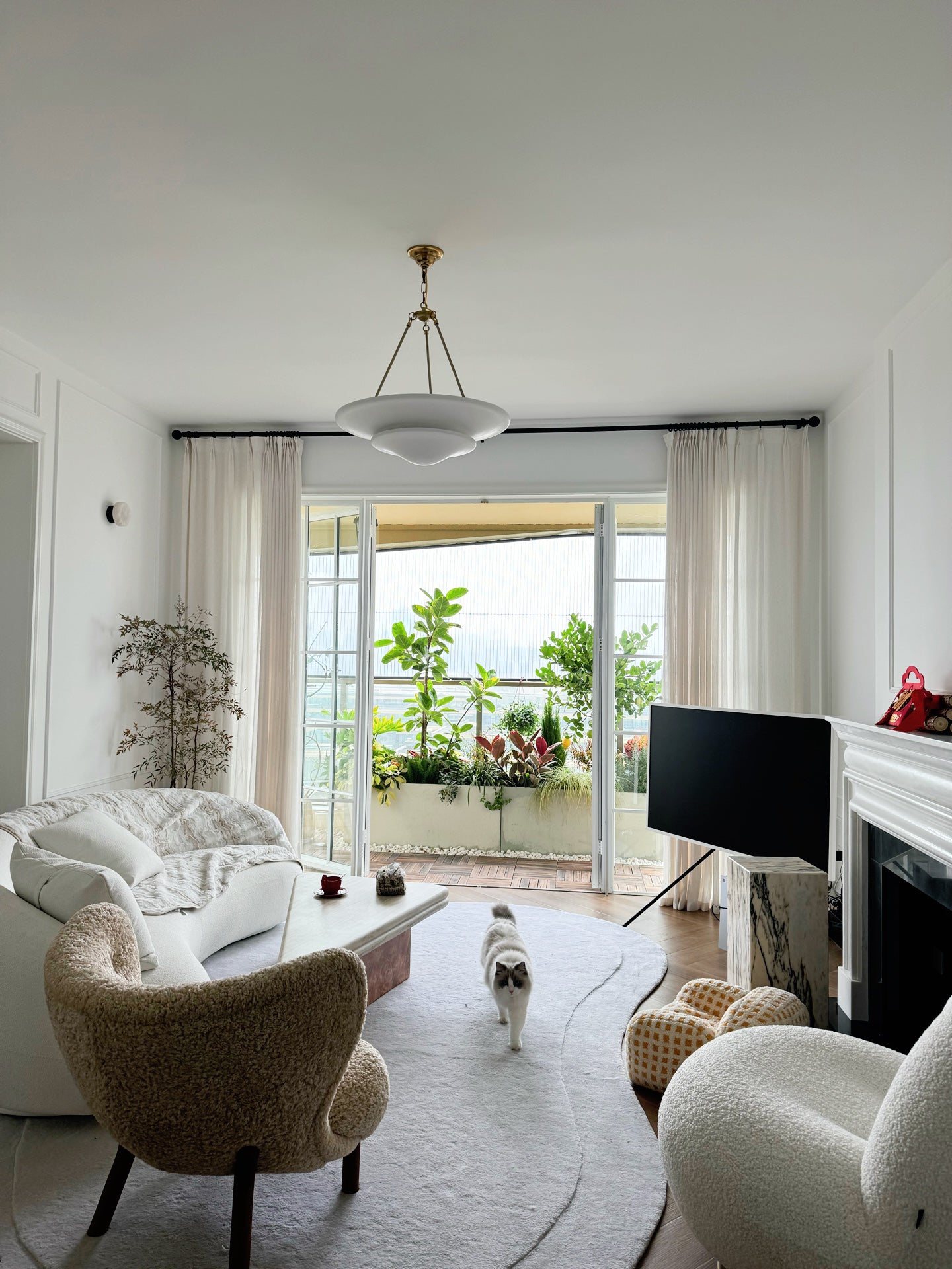 White Mollino bowl chandelier with gold-tone supports and short chain in living room with sofa, TV and glass doors