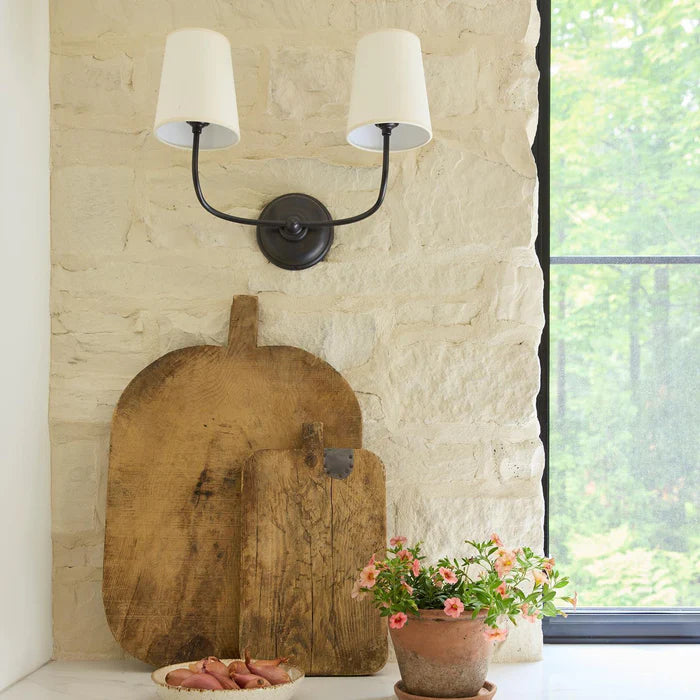 Black twin-arm wall light above wooden boards by a kitchen window.