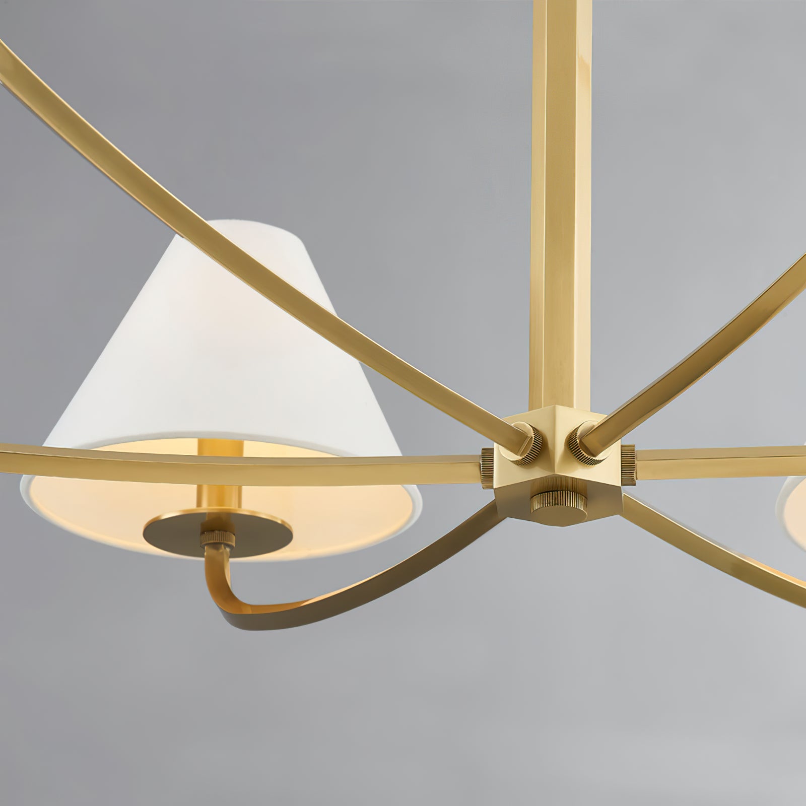 Close-up of Stacey gold-tone central hub, curved flat arms, ribbed joint fasteners and partially lit white shade