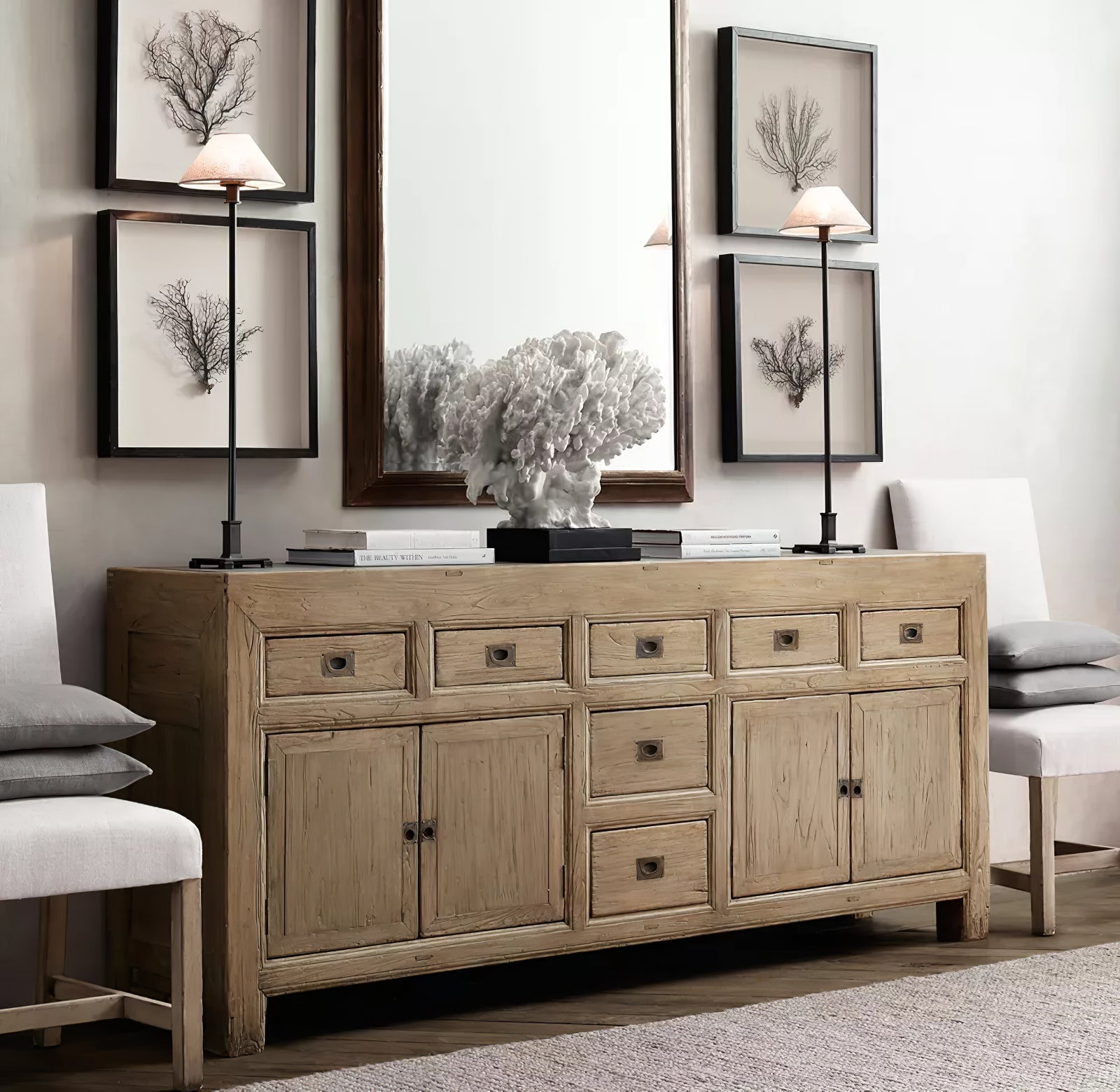 Two black-stem Slim Candlestick lamps with light shades on wood sideboard beside books and coral sculpture before mirror
