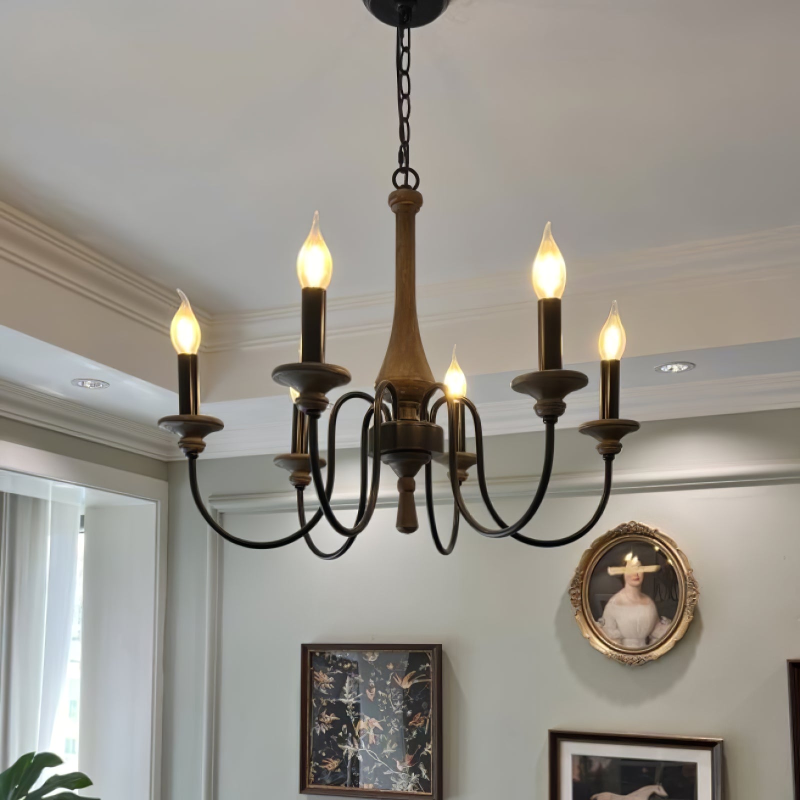 Lit wood-toned chandelier with black curved arms and chain before a wall of framed artwork