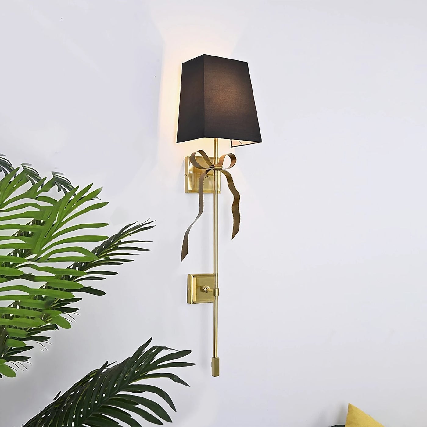 Black square-shade Ellery sconce on a pale wall beside green foliage