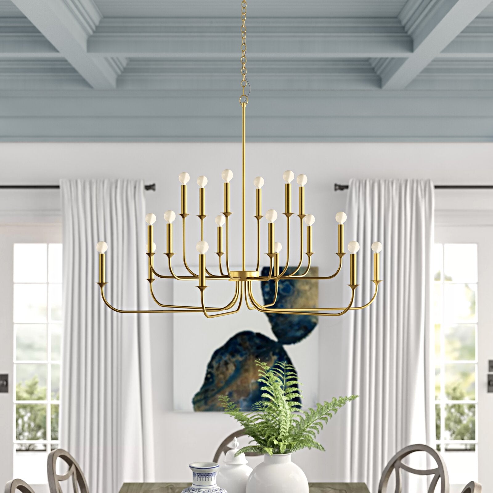 Gold multi-arm chandelier with white round bulbs above a dining table in front of blue-and-gold artwork