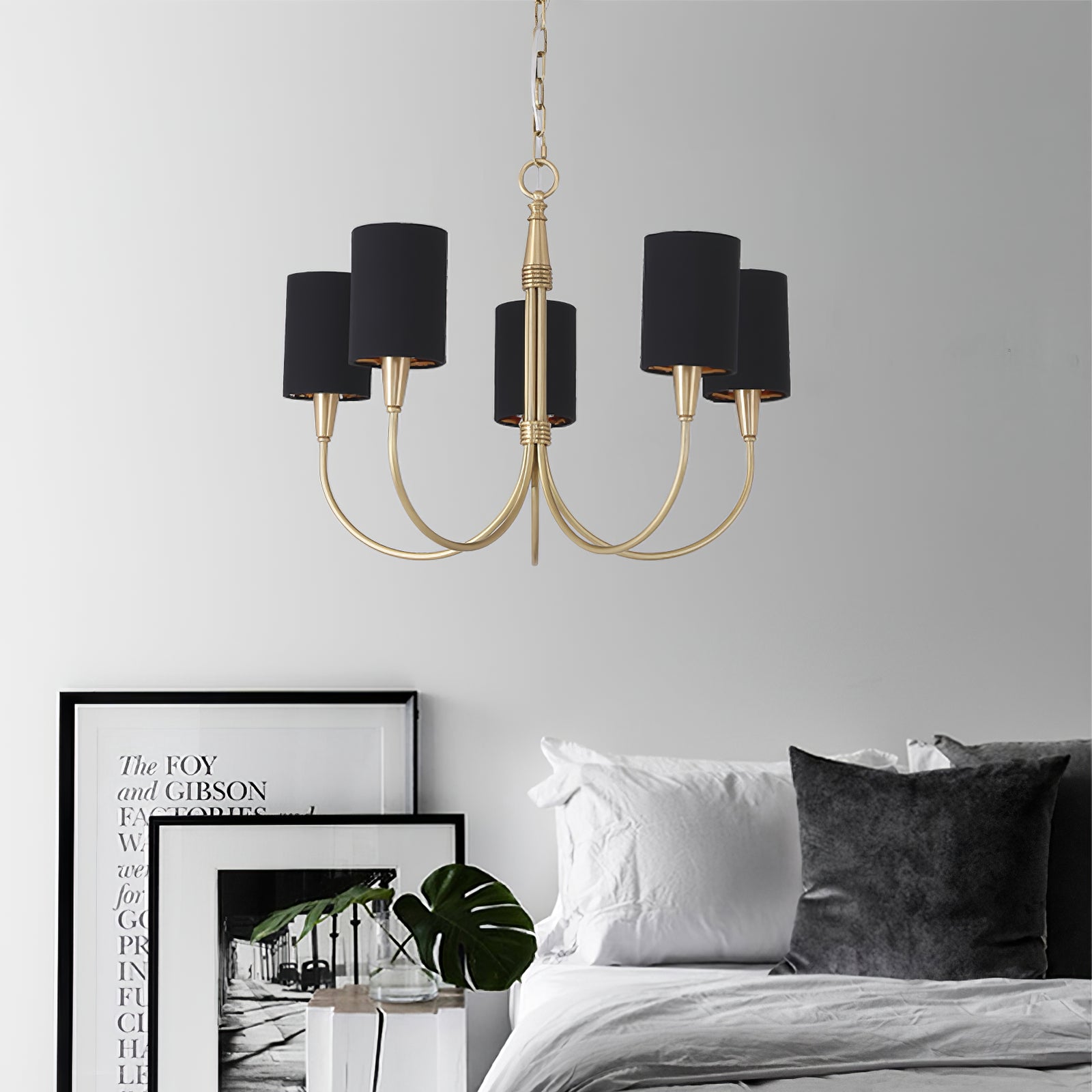 Five-light Black Quincy chandelier with gold-tone curved arms above a bed with grey and white pillows and framed prints