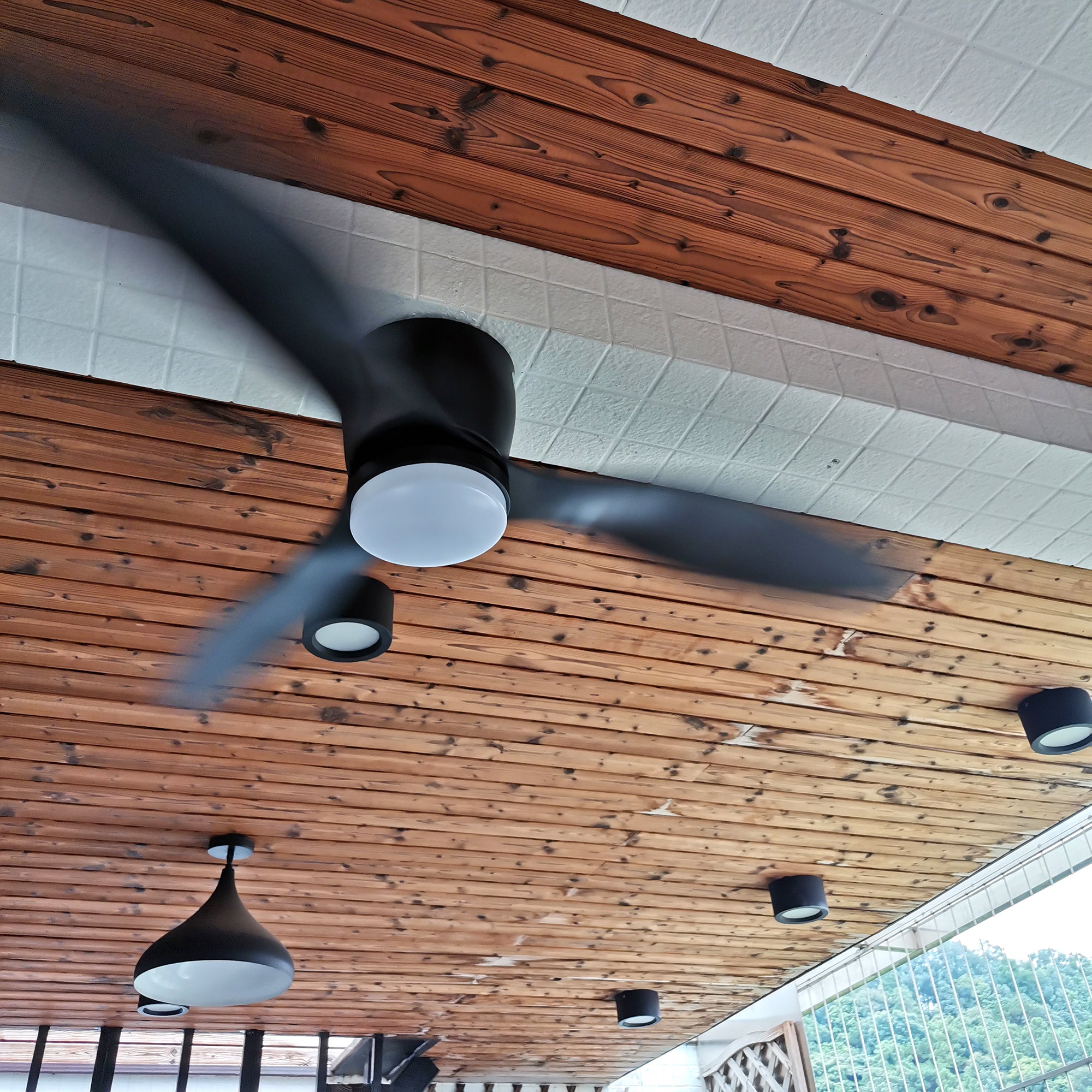 Multiple Black fans beneath a covered wooden ceiling