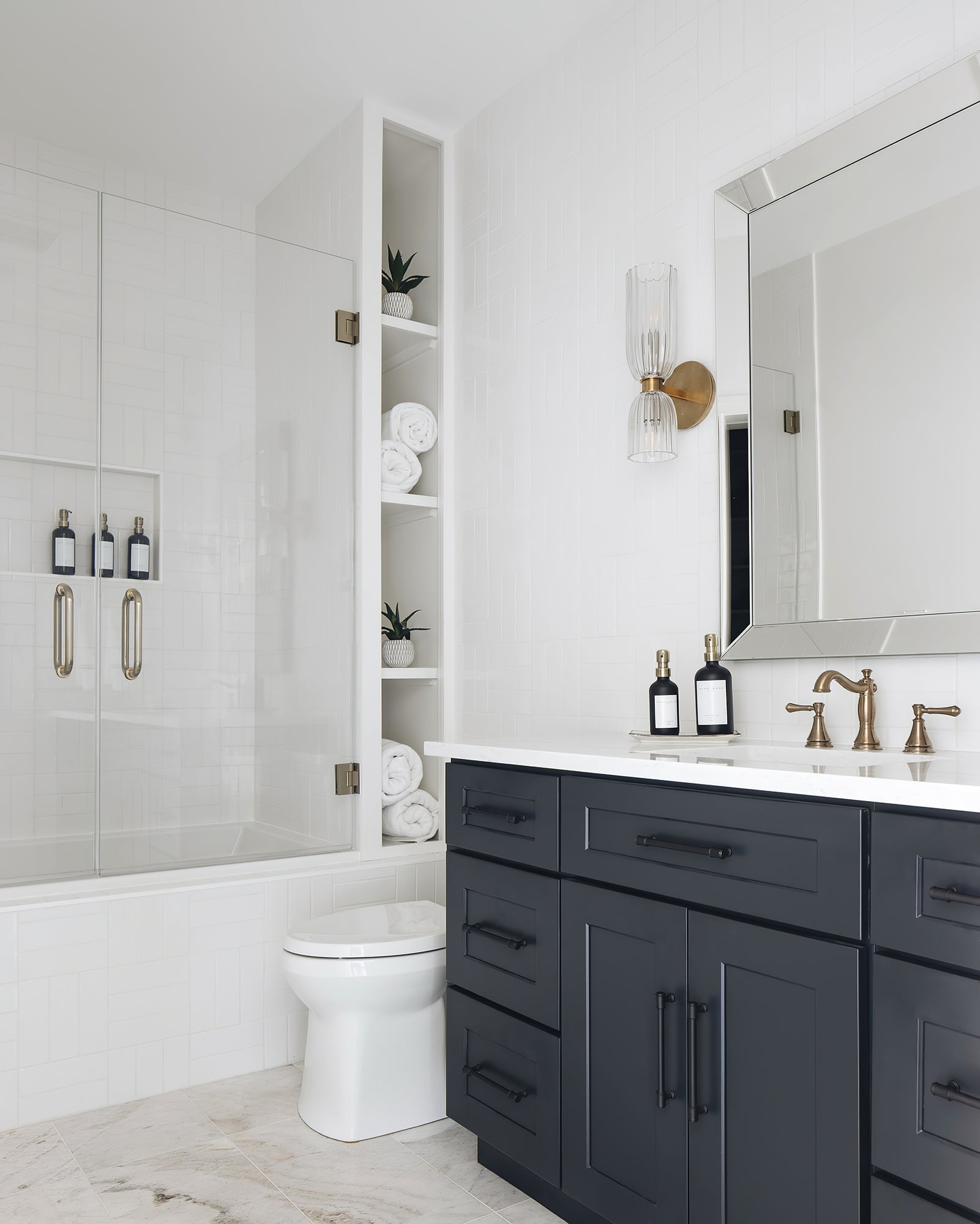 Double ribbed glass sconce beside a silver-bordered mirror above a blue vanity near white brick tiles
