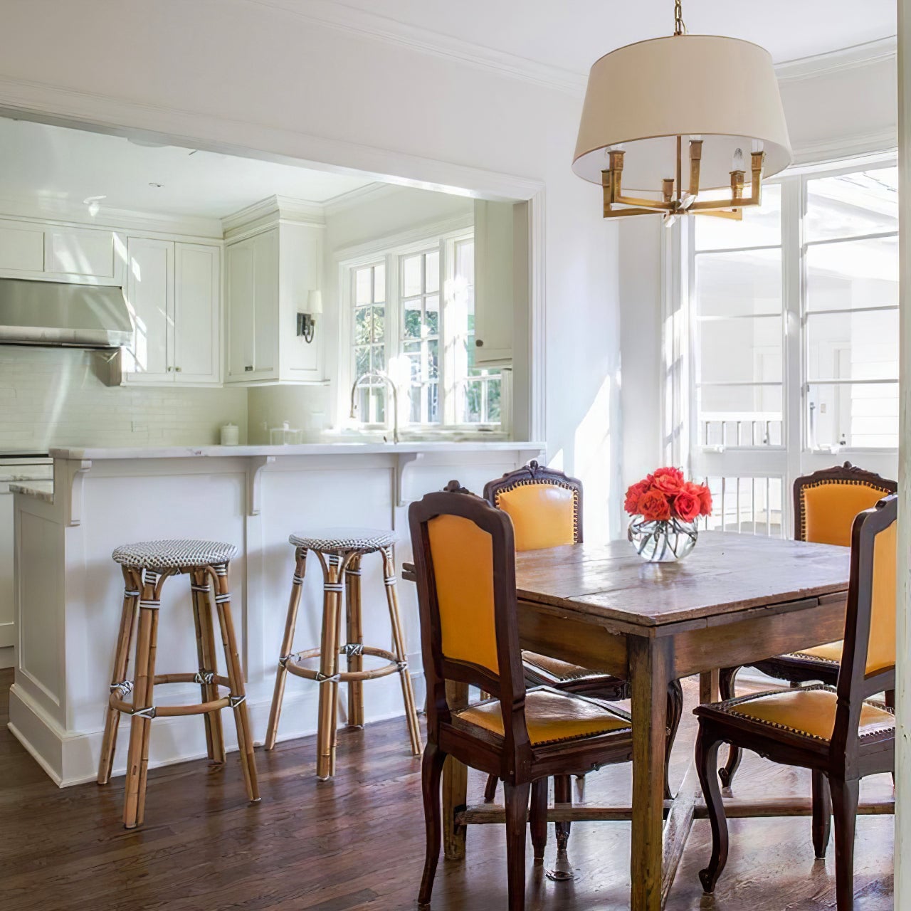 Gold-toned shaded chandelier above a wooden dining table with yellow chairs and red roses