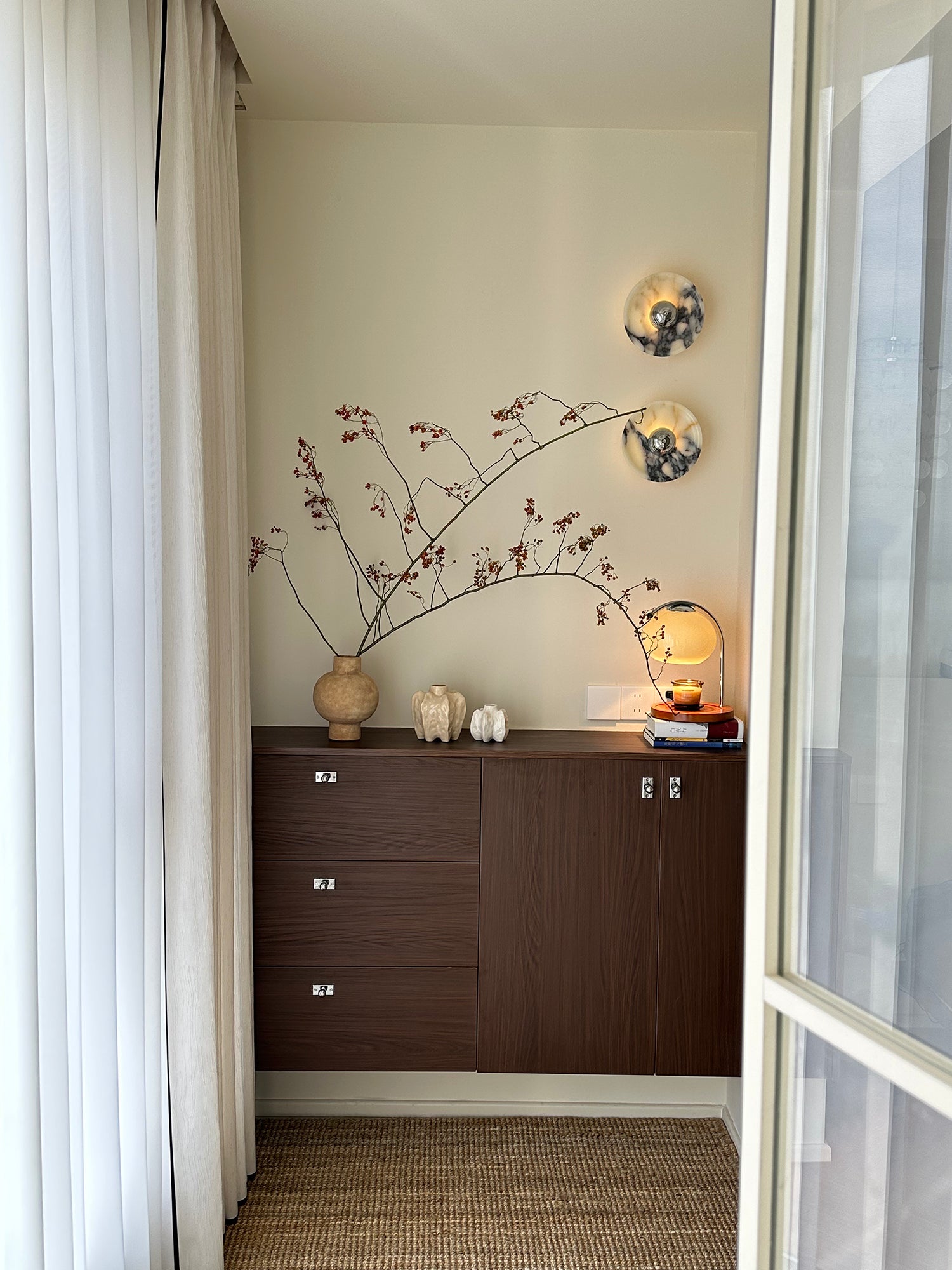 Two Silver-centred veined stone wall lights above a wood cabinet with branches, pottery and a separate table lamp