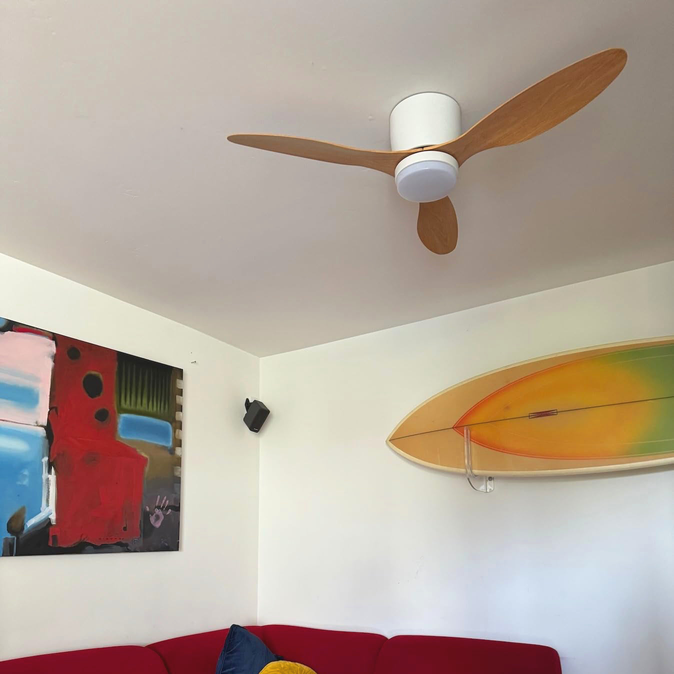 Wood-toned fan blades above a red sofa and surfboard