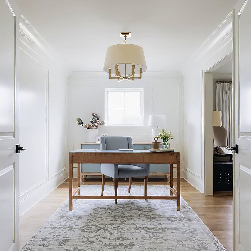 Gold-toned shaded chandelier above a desk and grey chair, viewed through white double doors