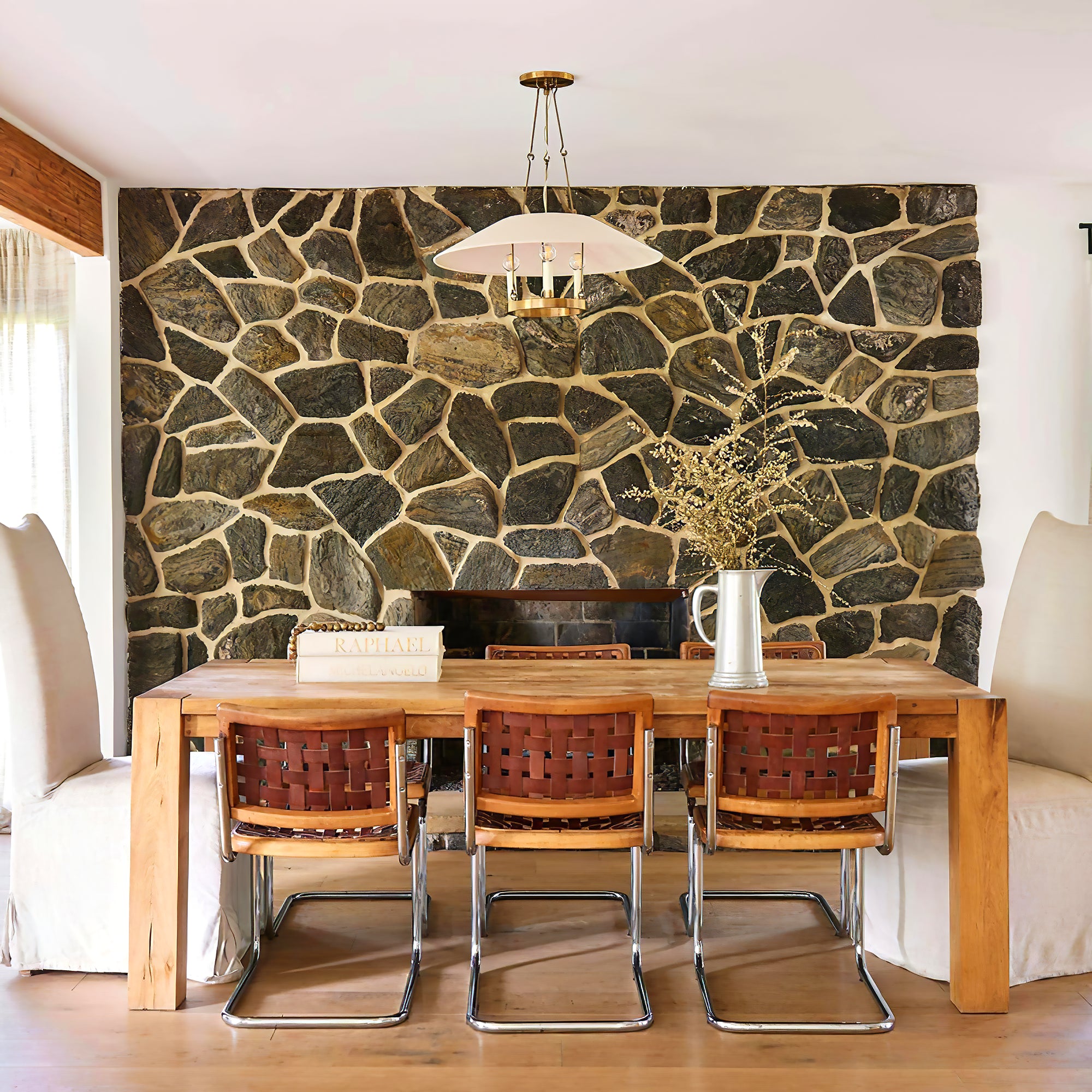Troy Archive chandelier above a wooden table beside a stone wall