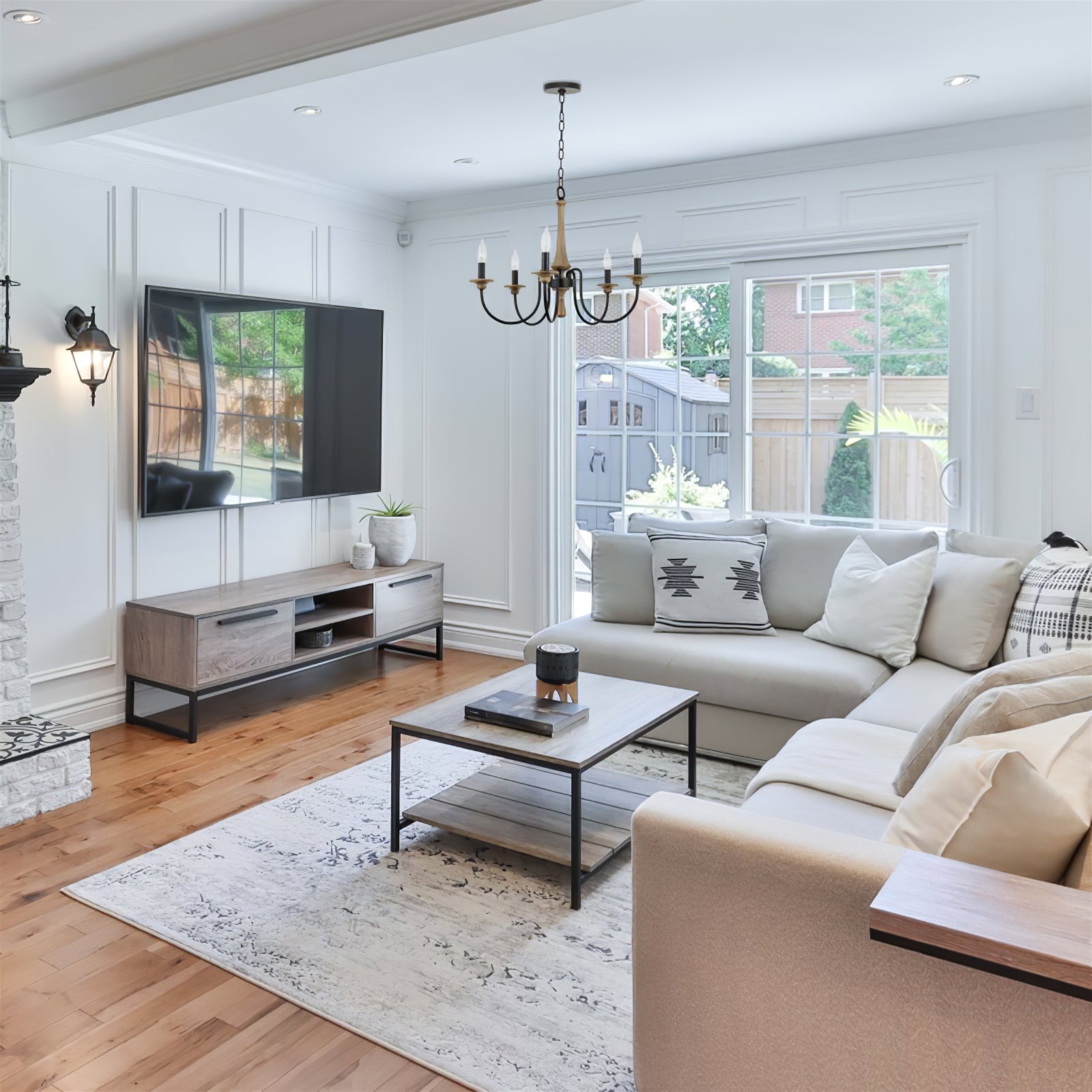 Five-light wood-toned chandelier in a bright living room with white sectional sofa and wooden TV console