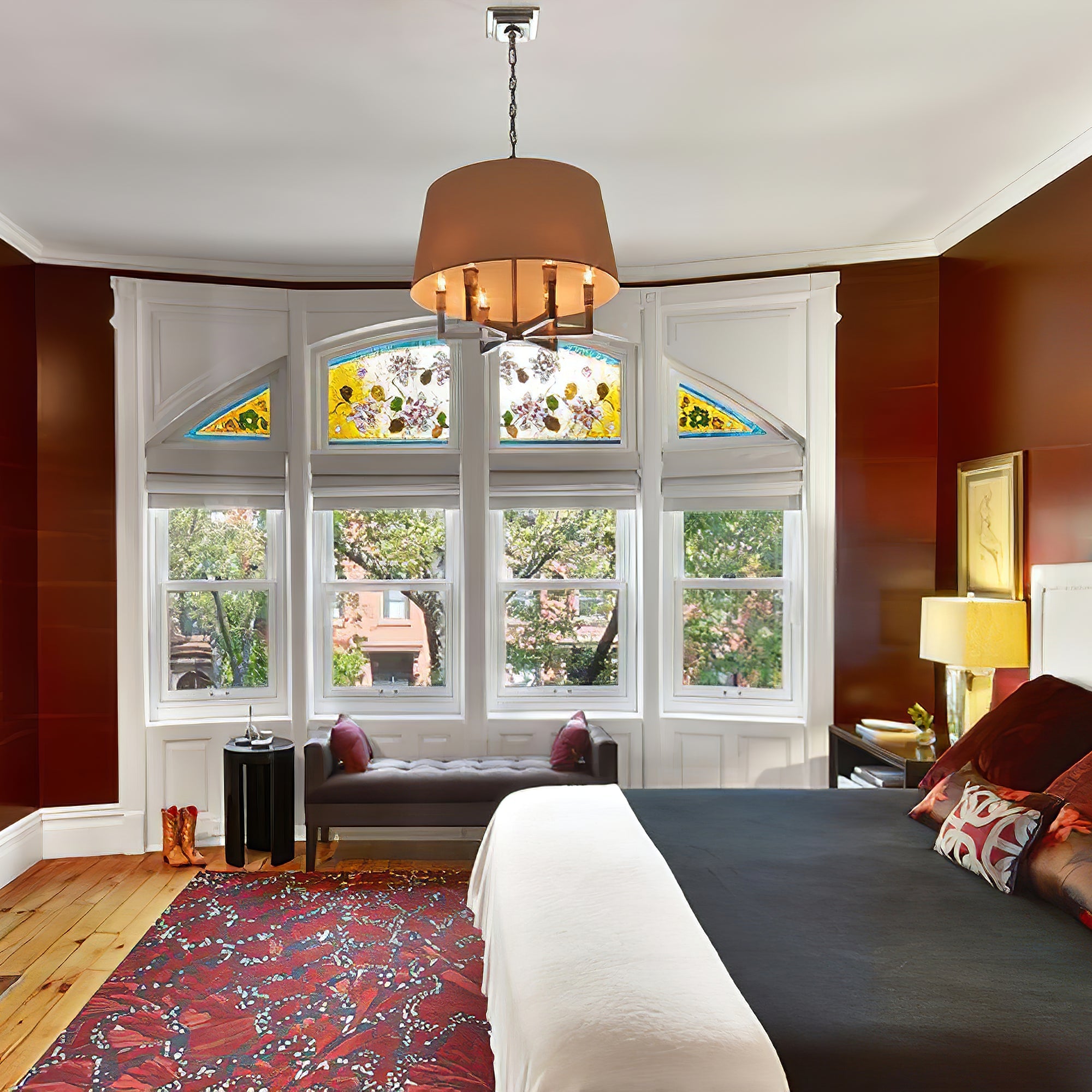 Illuminated tan-looking chandelier shade in a red bedroom with stained-glass window, bed and chaise