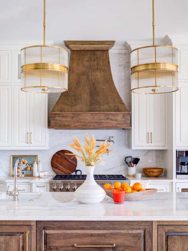 Two bronze-tone glass-rod drums by a wood range hood, with a wheat vase and orange cup on the island