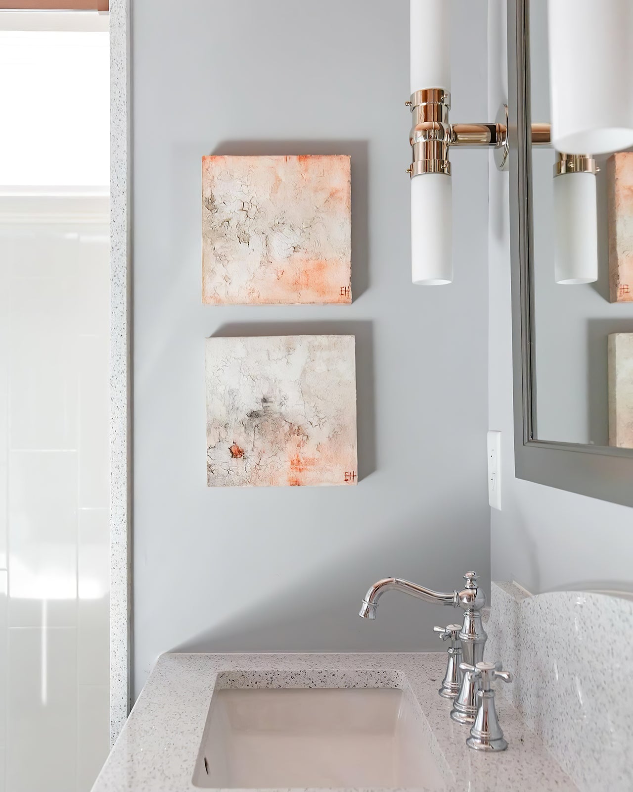 Close silver-tone central cylinder and short arm beside a mirror, abstract pictures and a basin tap