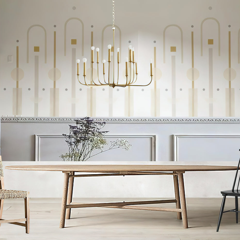 Gold multi-arm chandelier above an oval wooden dining table in front of pale patterned and paneled walls