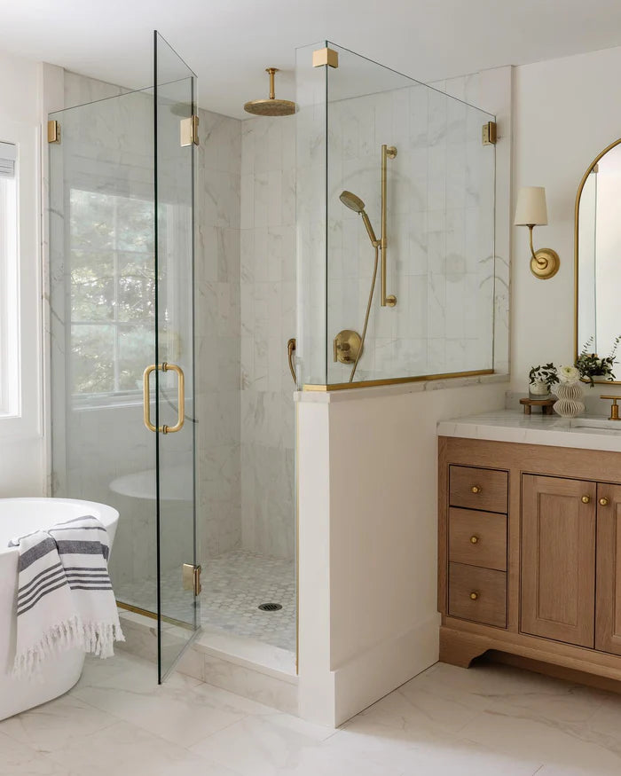 Brass single-shade wall light beside a vanity mirror near a glass shower enclosure.