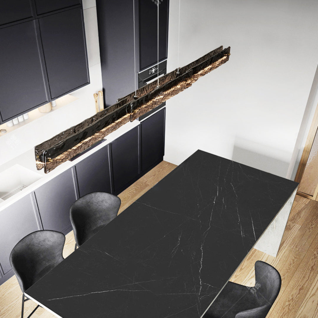 High-angle view of dark-framed glass pendant above a dark kitchen island with grey stools and dark cabinets