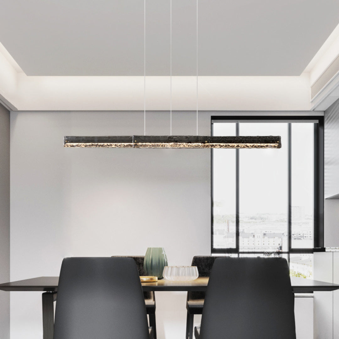 Dark-framed linear pendant above a dining table near tall windows, with green vase and dark chairs