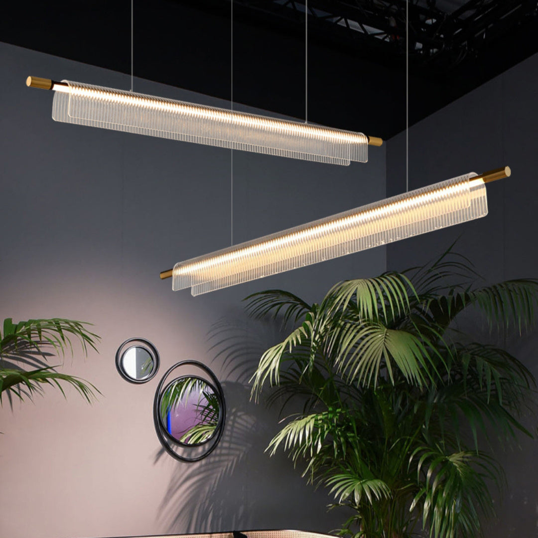 Two illuminated ribbed acrylic linear pendants in a dark interior with palms and circular mirrors