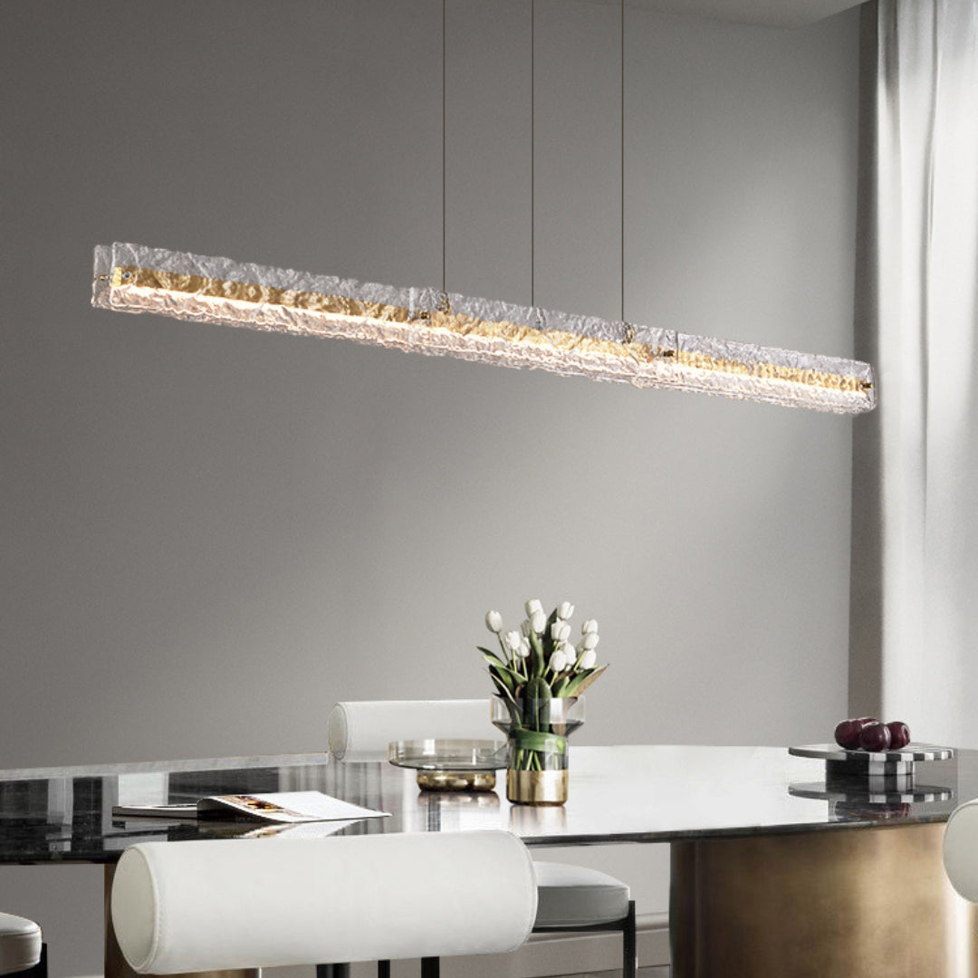Capuccio Gold + Clear linear pendant above a reflective table with white chairs and white tulips