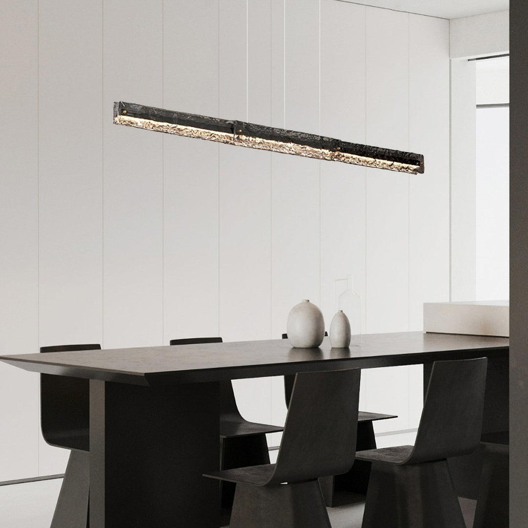 Dark-framed lit glass pendant above a dark dining table with angular chairs and two pale vases