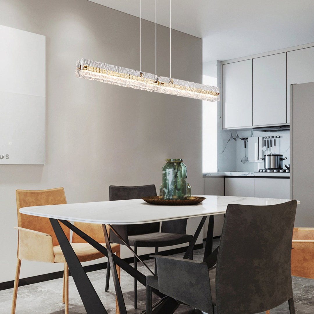 Capuccio Gold + Clear pendant above a pale table with mixed chairs and green vase, with kitchen behind