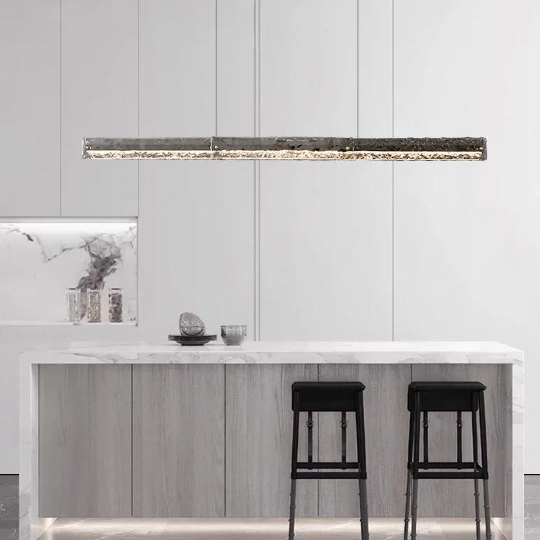 Dark-framed textured-glass pendant above a pale island with two black stools and white wall panels