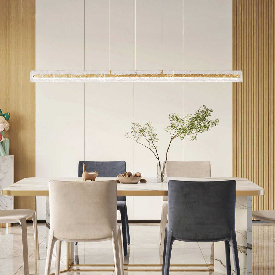 Gold-toned textured-glass pendant above a pale dining table with beige and dark chairs and leafy branches