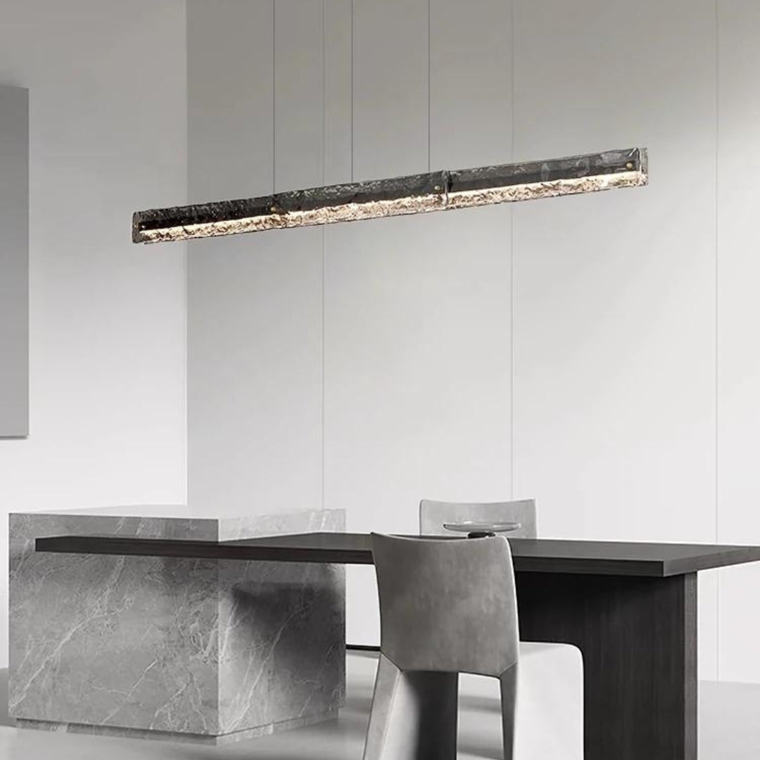 Dark-framed textured-glass pendant above a narrow dark dining table with grey chair and stone-pattern block