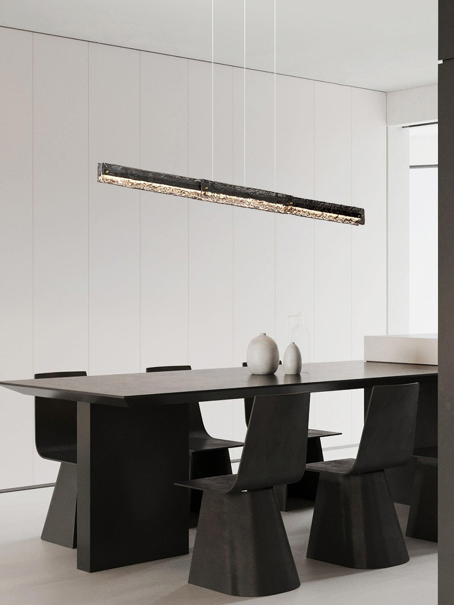 Dark rectangular lit pendant above a dark dining table and two pale vases against a light wall