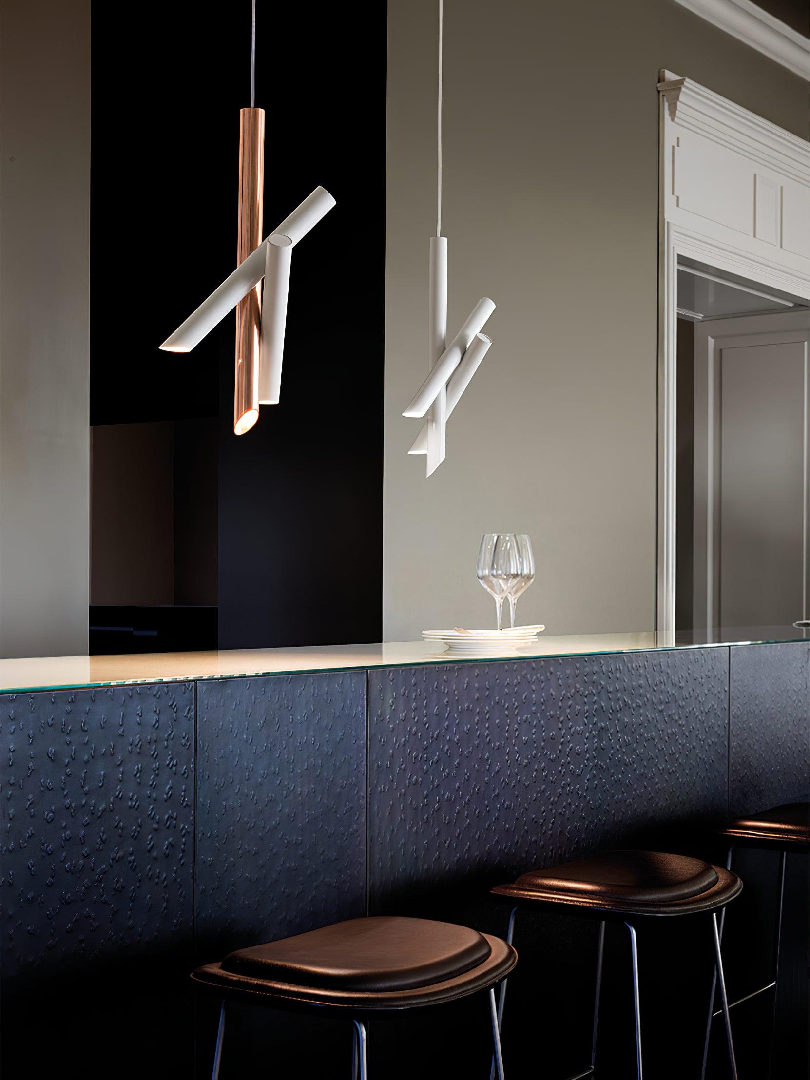 White and rose-gold Tubes pendants above a dark upholstered bar bench, with reflections in the mirror