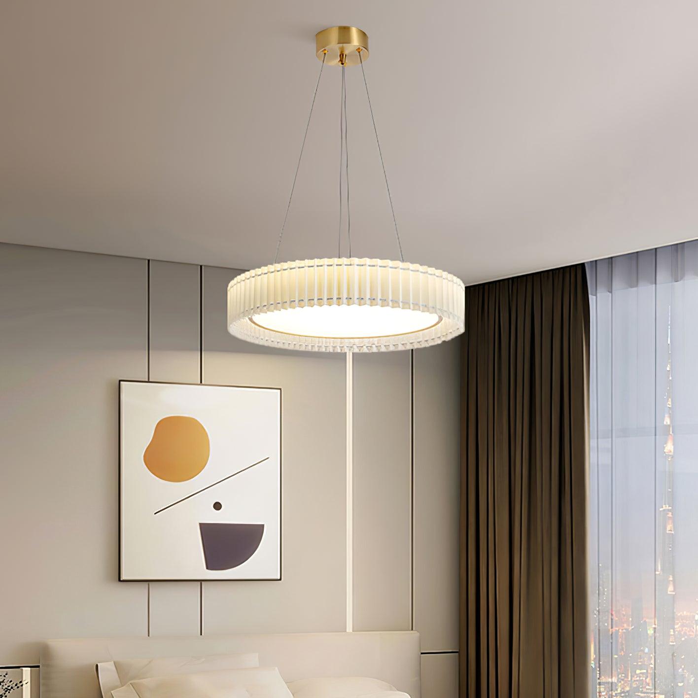 Lit round pleated pendant above a bed with white pillows and abstract orange-and-gray wall art