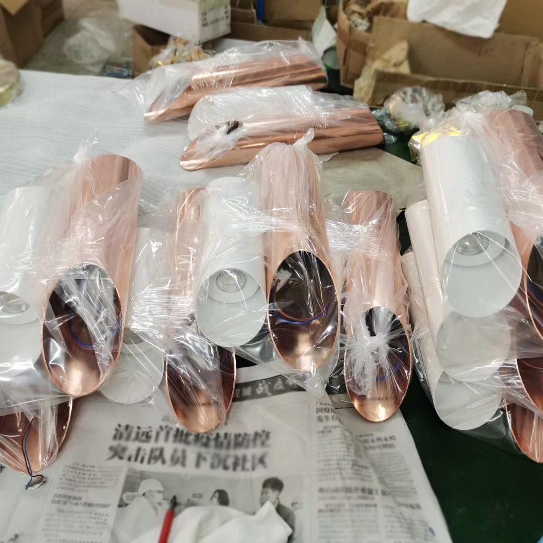 Plastic-wrapped white and rose-gold tubular light components laid on a work surface