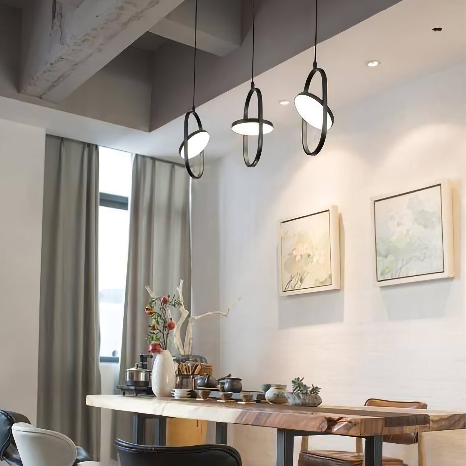 Three black oval pendants above a dining table in a bright room