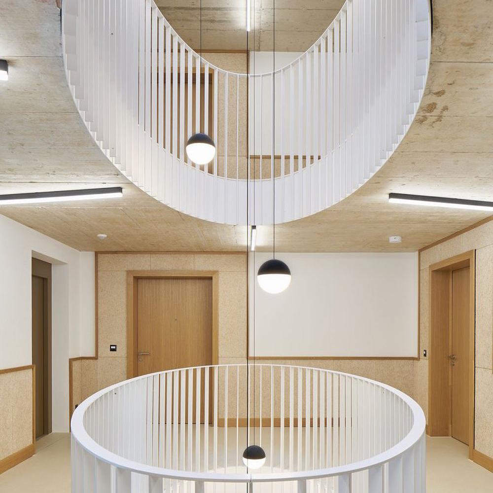 Black-top pale-lower globe pendants at different drops in a circular stairwell with white rails and wood doors