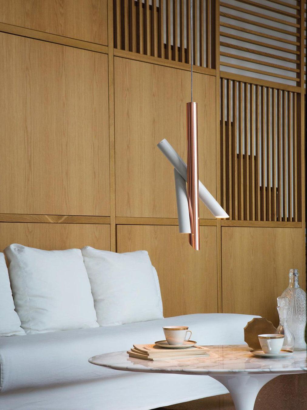 White and rose-gold Tubes pendant in front of wooden wall panels above a cushioned bench