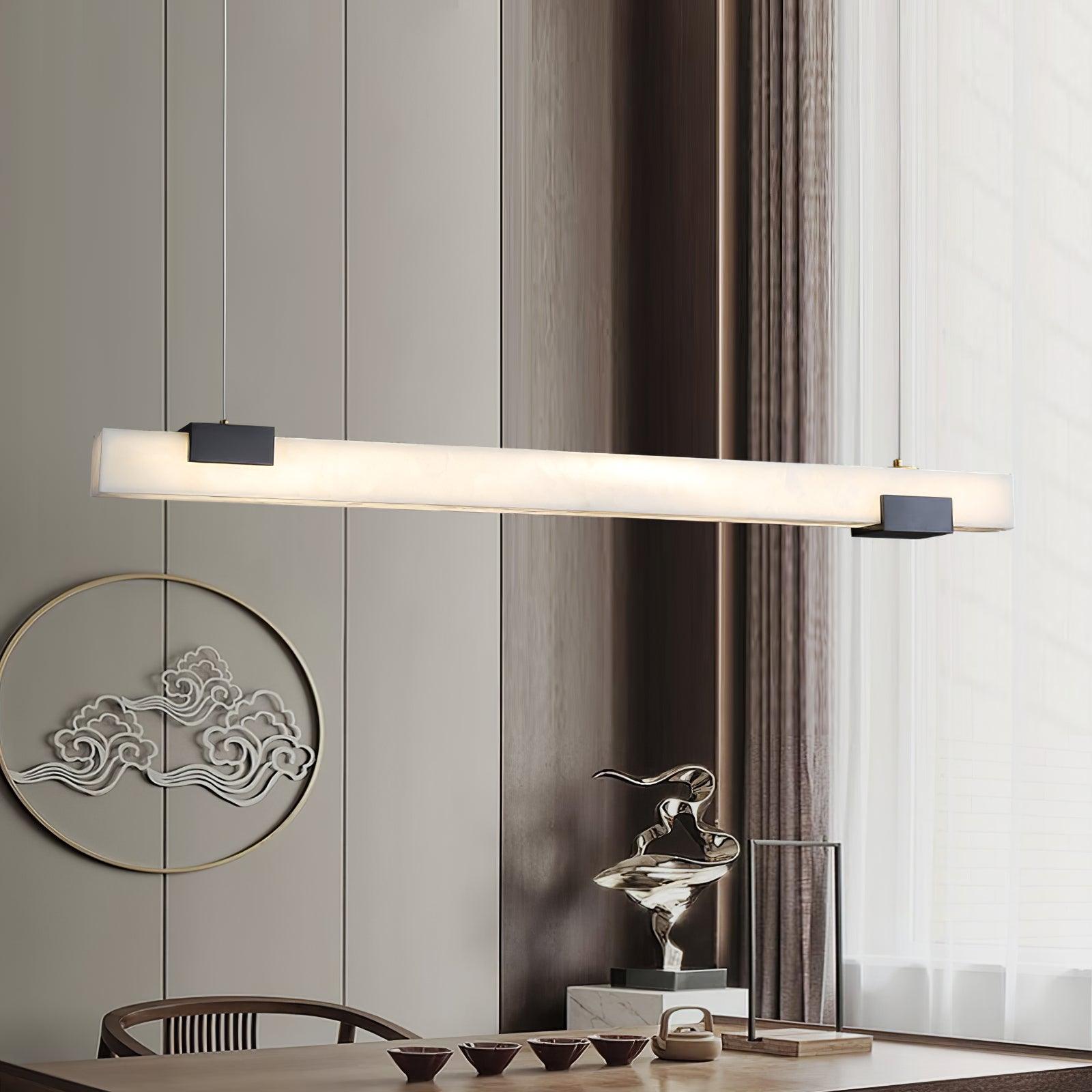 Glowing white linear pendant above a wooden dining table with tea cups, round wall artwork and curtains