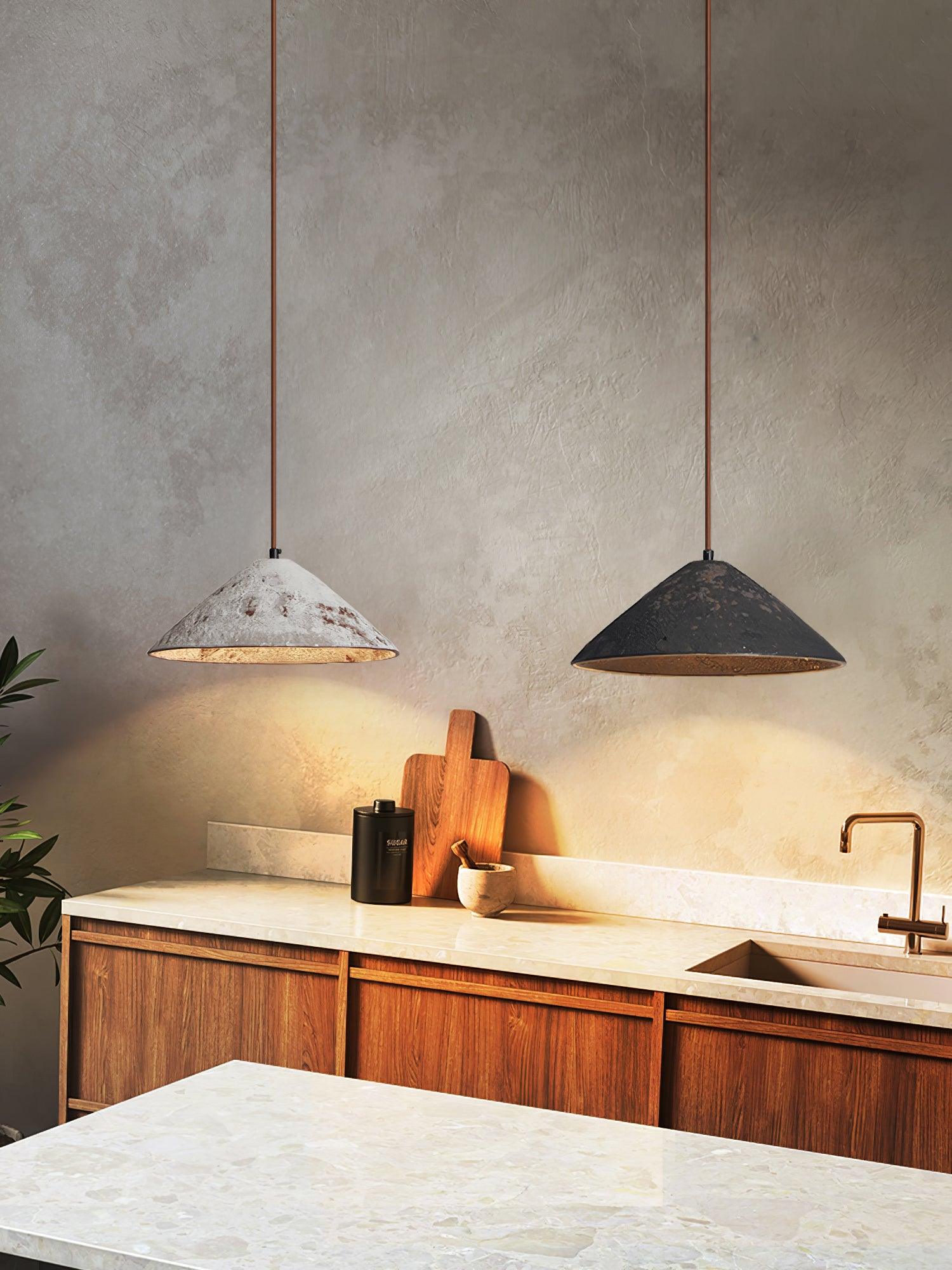 White and black cone pendants above a wood kitchen cabinet and pale counter with cutting board, canister and faucet