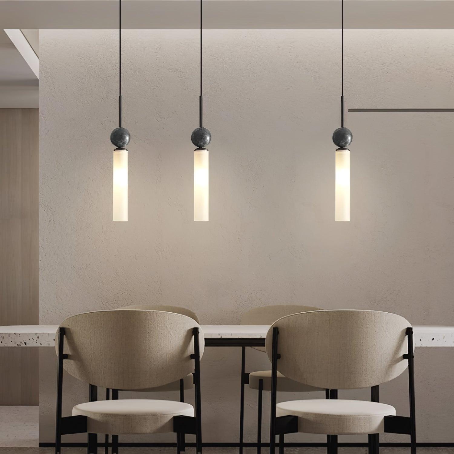 Three black-stem marble-sphere pendants with glowing white tubes above a dining counter and pale upholstered chairs