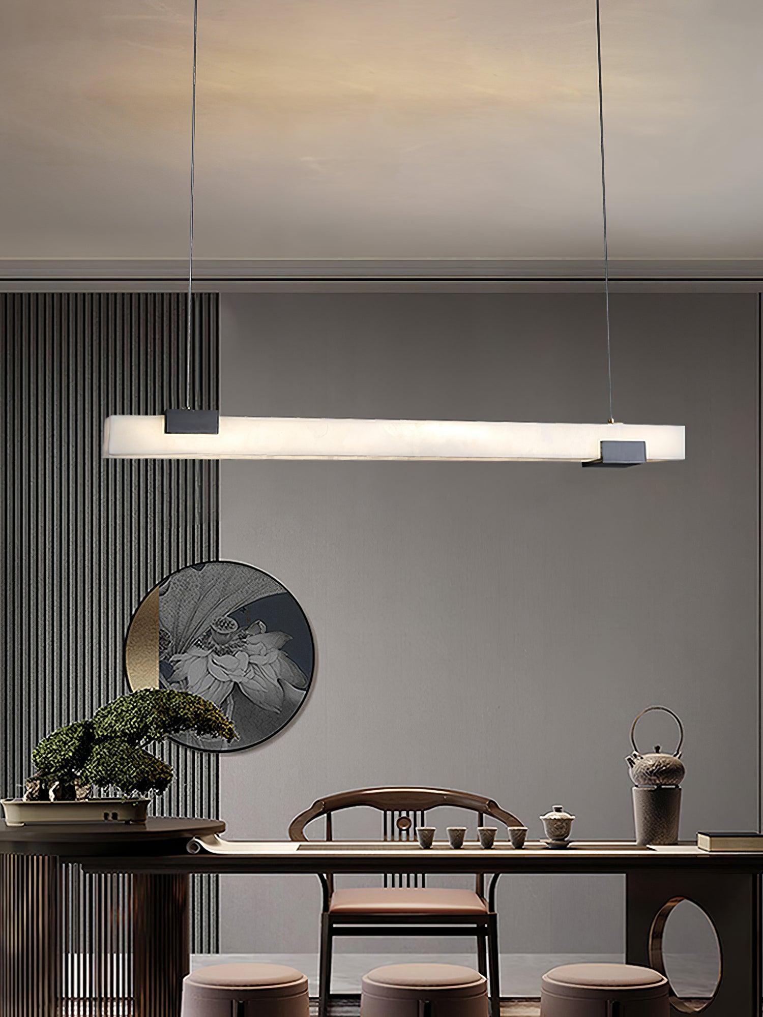 Wide tea-area view with white bar pendant, dark table, wooden chair, three upholstered stools and round wall artwork