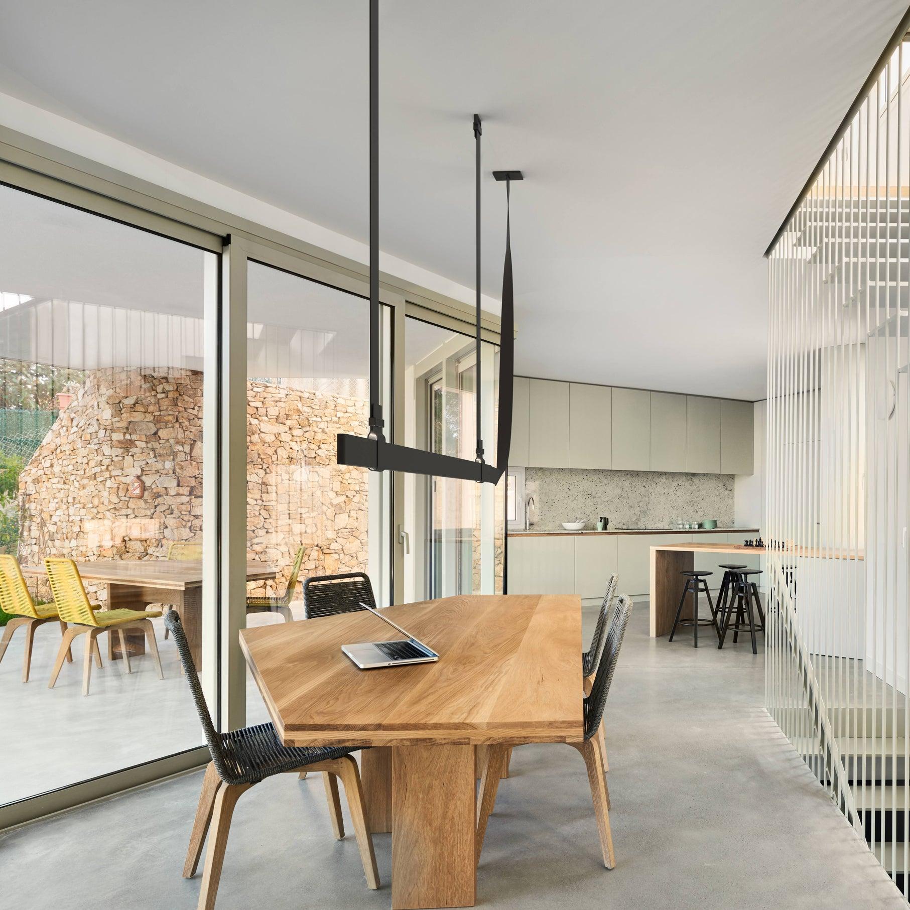 Black linear pendant above a table beside a window