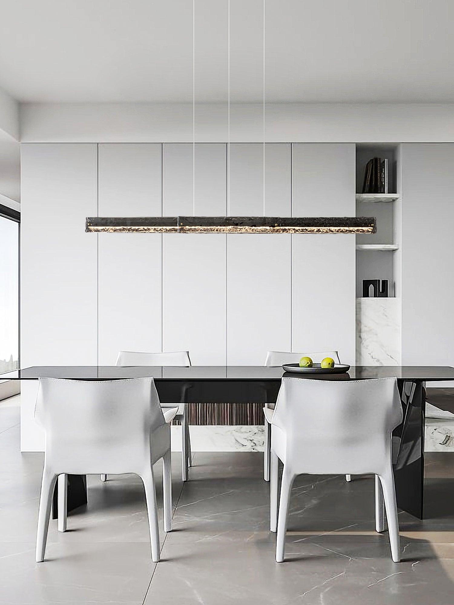 Dark rectangular textured pendant with lit lower strip above a black dining table and white chairs