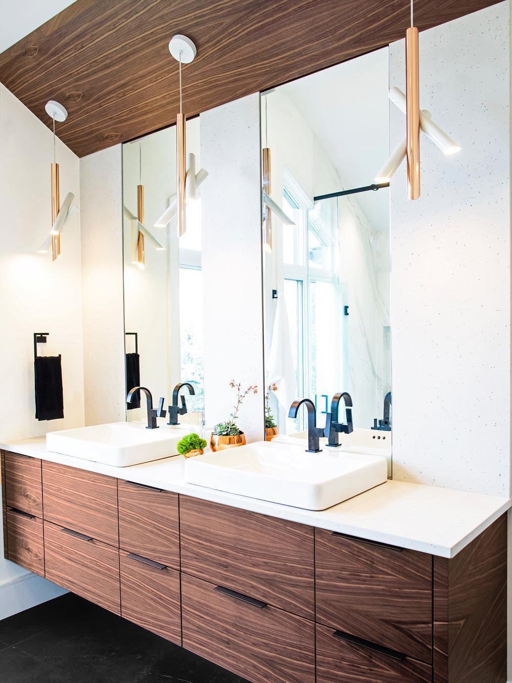 White and rose-gold Tubes pendants and mirror reflections above two washbasins and a wooden vanity