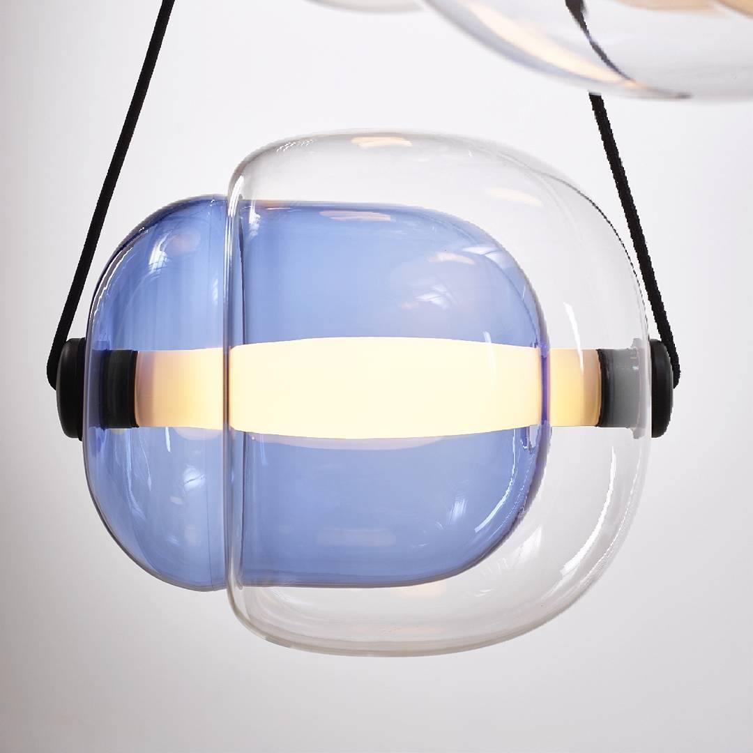 Blue inner glass inside the clear Capsula shade, crossed by a luminous tube and held by two dark straps