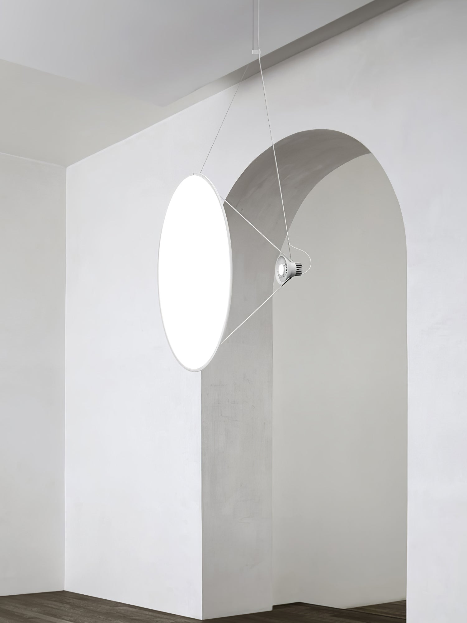 Single white disc pendant suspended vertically beside a grey archway