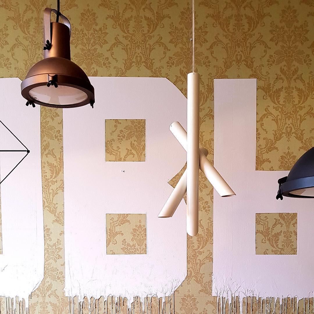 White and rose-gold Tubes pendant in a display with other lights against a patterned wall