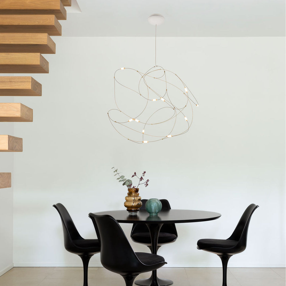 Compact lit wire-loop pendant above a round black dining table with black chairs