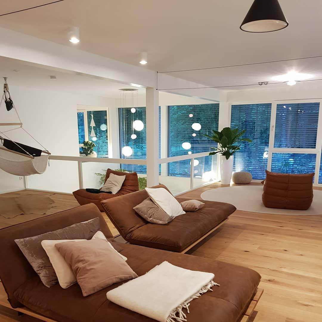 Black conical shade and cable above brown lounge chairs with cream cushions, a hammock and large windows