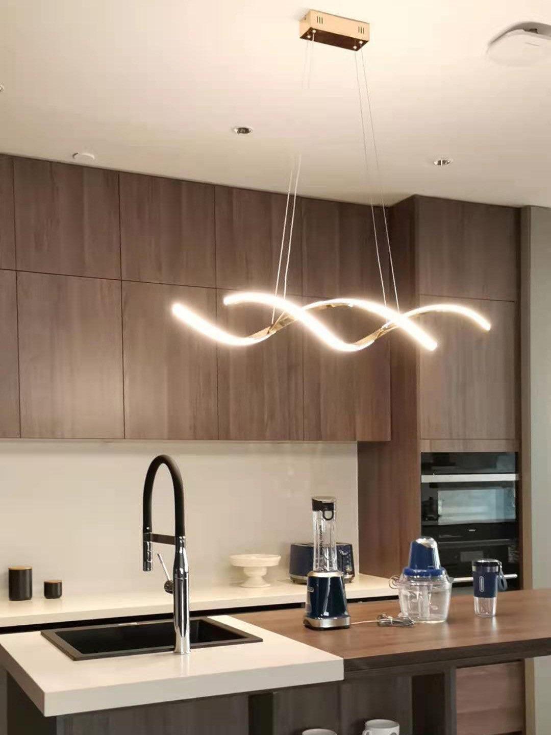 Glowing gold wave pendant above a kitchen sink and wood cabinets